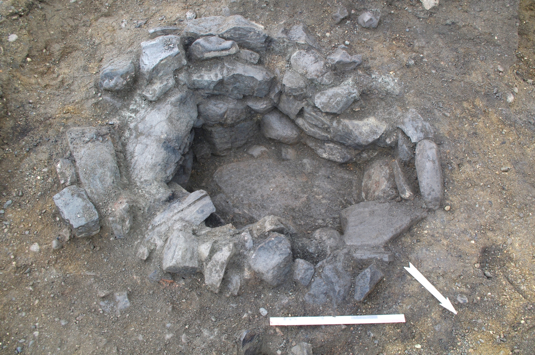 Hjørneildstedet etter at alle steiner over gulvflaten i grophuset er fjernet. Ovnen har oval grunnform, og har en flat skiferhelle i bunnen. Foto: Marte Mokkelbost, NTNU Vitenskapsmuseet.
