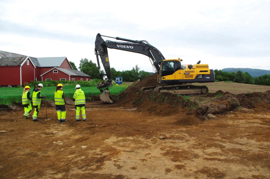 Heidi, Kristoffer, Isabella og Kari foran en av gravemaskinene som brukes til &aring; fjerne matjorda. Foto: Marte Mokkelbost, NTNU Vitenskapsmuseet.